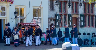 Kanoniers in Veere Historische reenactors in uniform met geweren, staan bij een oude gevel.