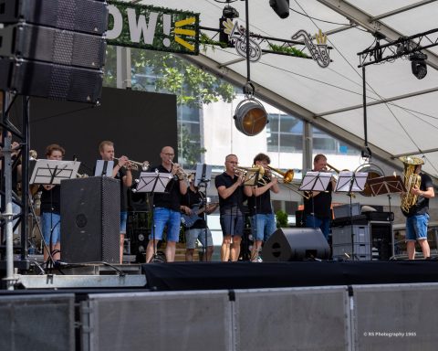 BLOW optreden centrum kerkrade Een blaasorkest speelt op een podium onder een tent met muziekstandaards.