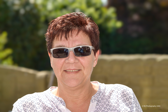 Een moment portret Jolanda Vrouw met korte bruine haren in een witte blouse en zonnebril, glimlachend.