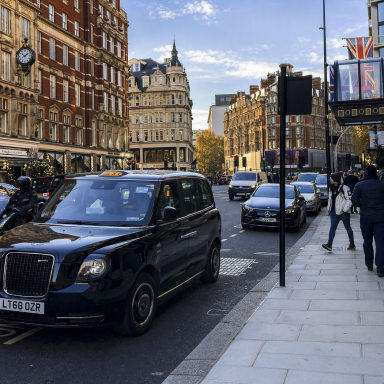In London Black Cab Drukke straat met zwarte taxi's en historische gebouwen onder een blauwe lucht.